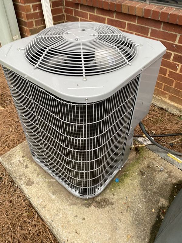 Gray outdoor AC condenser on a concrete pad beside a brick home